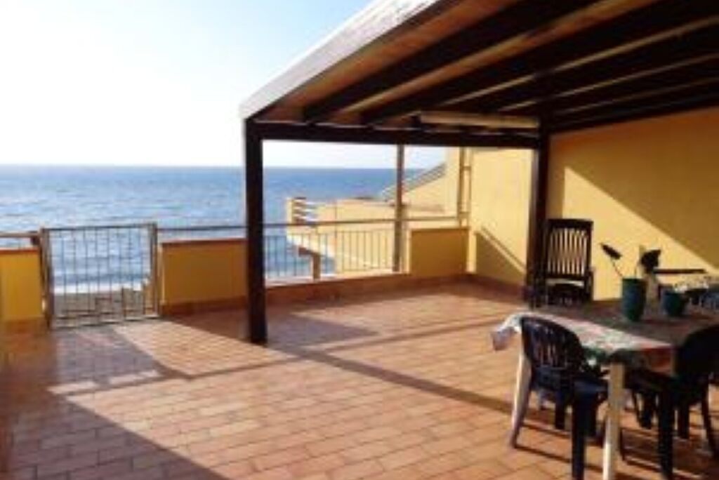 Un espacio al aire libre techado con una mesa y sillas, vista al mar y baranda.