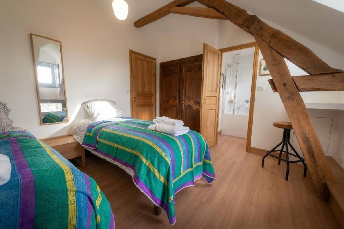 Ein Schlafzimmer mit zwei Betten, Holzbalken, einem hölzernen Hocker und einem Spiegel.