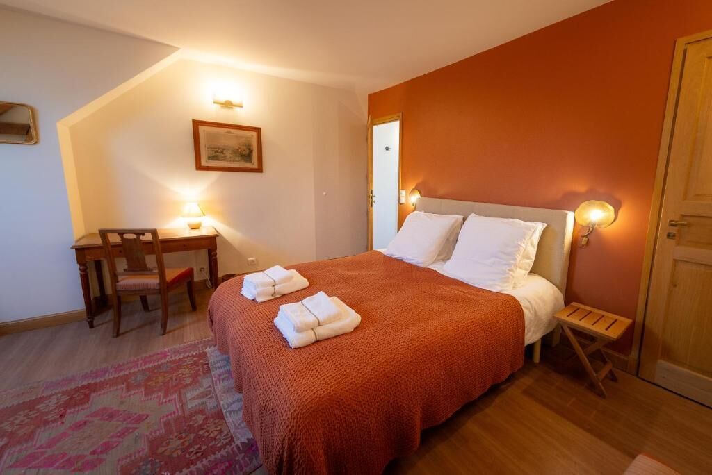 Ein Schlafzimmer mit einem Bett, einem Schreibtisch und einem Stuhl. Auf dem Bett liegen Handtücher und auf dem Boden ein Teppich.