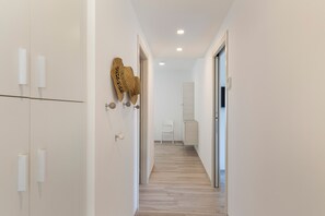 Ein schmaler Flur mit Holzboden, weißen Wänden und einem weißen Stuhl in der Ferne.