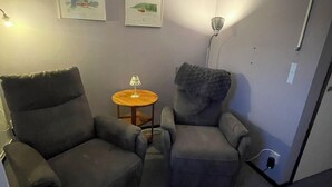 A room with two grey armchairs, a small wooden table, and two framed pictures on the wall. - Åre Vandrarhem (Duved)