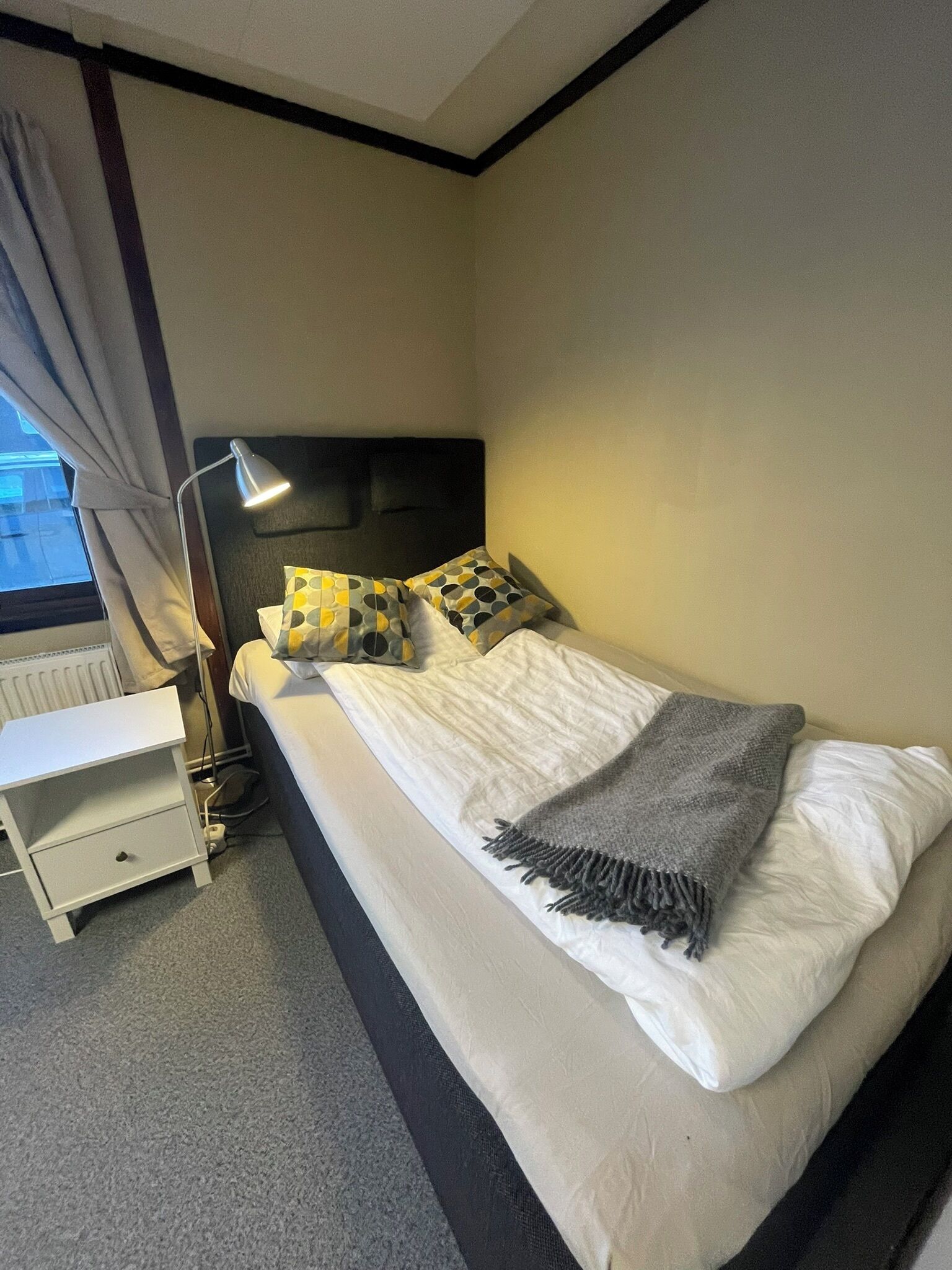 A neatly made bed with pillows, a bedside lamp, and a small white nightstand.