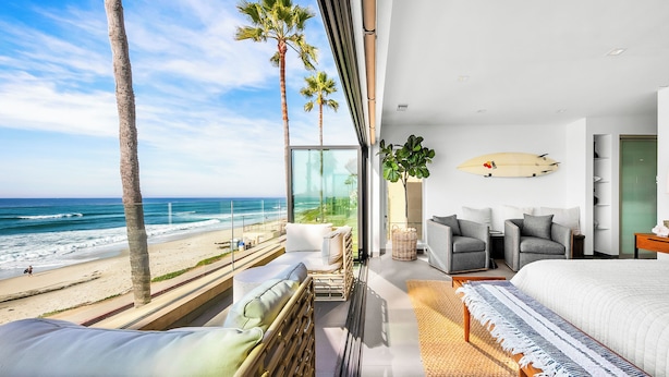 Une chambre moderne avec un grand lit, une vue sur la plage et une planche de surf accrochée au mur.