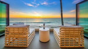 Un balcon avec des fauteuils en osier et une table ronde, donnant sur une plage au coucher du soleil.