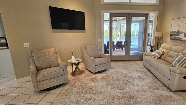 A living room with two armchairs, a sofa, a flat-screen TV, a painting, and a view through a glass door to an outdoor area.