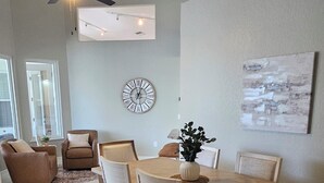 A dining area with a wooden table and chairs, a ceiling fan, and a large wall clock.