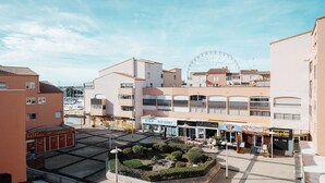 A coastal town with a central square featuring a café, a sushi restaurant, and a Ferris wheel in the background. - Charming Studio - Sleeps 2 - Close to the sea (Agde)
