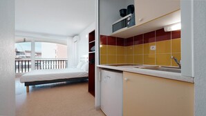 A compact room with a bed, a kitchenette with yellow and red tiles, and a balcony with a view. - Charming Studio - Sleeps 2 - Close to the sea (Agde)
