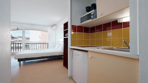 A compact room with a bed, a kitchenette with yellow and red tiles, and a balcony with a view. - Charming Studio - Sleeps 2 - Close to the sea (Agde)