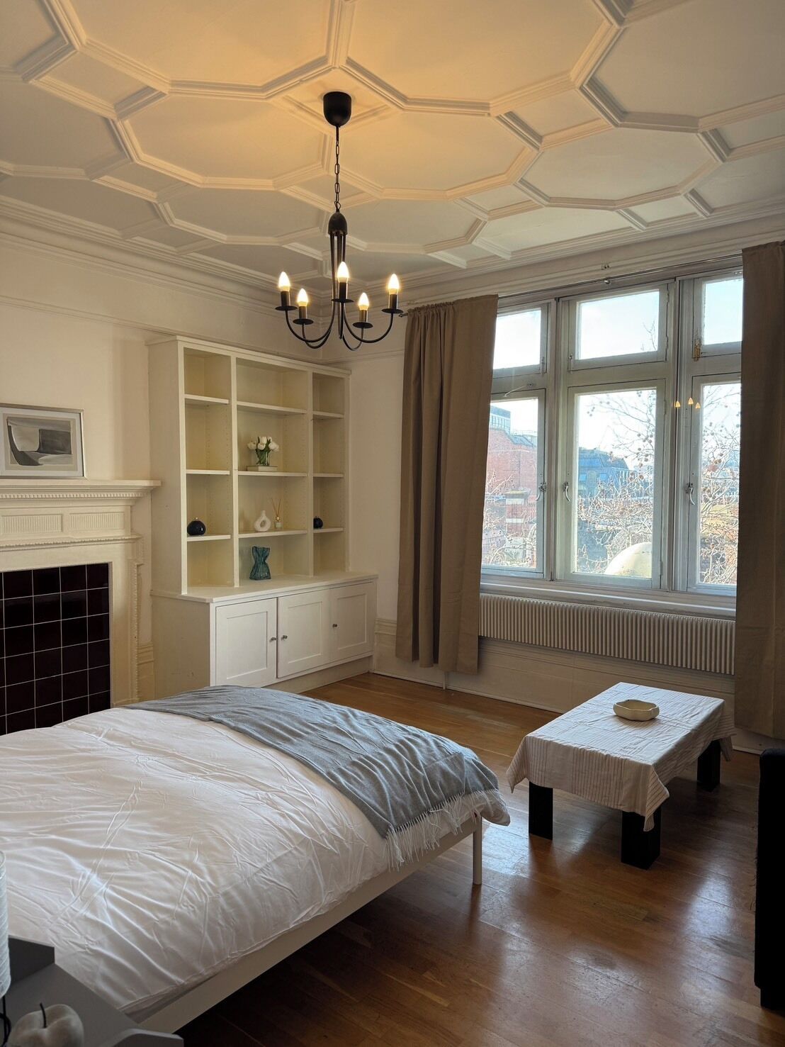 Une chambre à coucher avec un grand lit, une commode, une cheminée et une vue sur l’extérieur par une fenêtre.