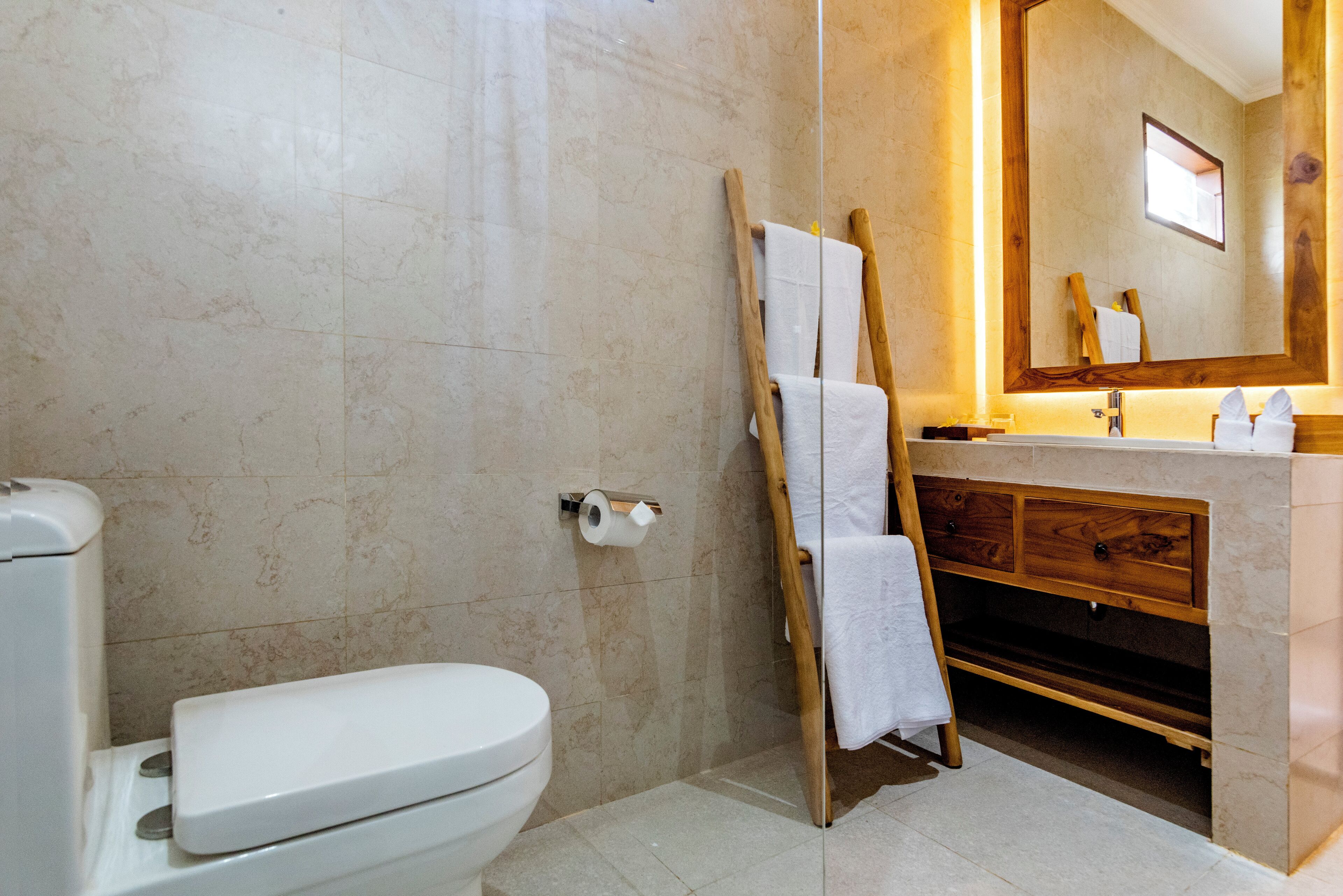 A bathroom with a toilet, a wooden vanity with a mirror, and a shower area.