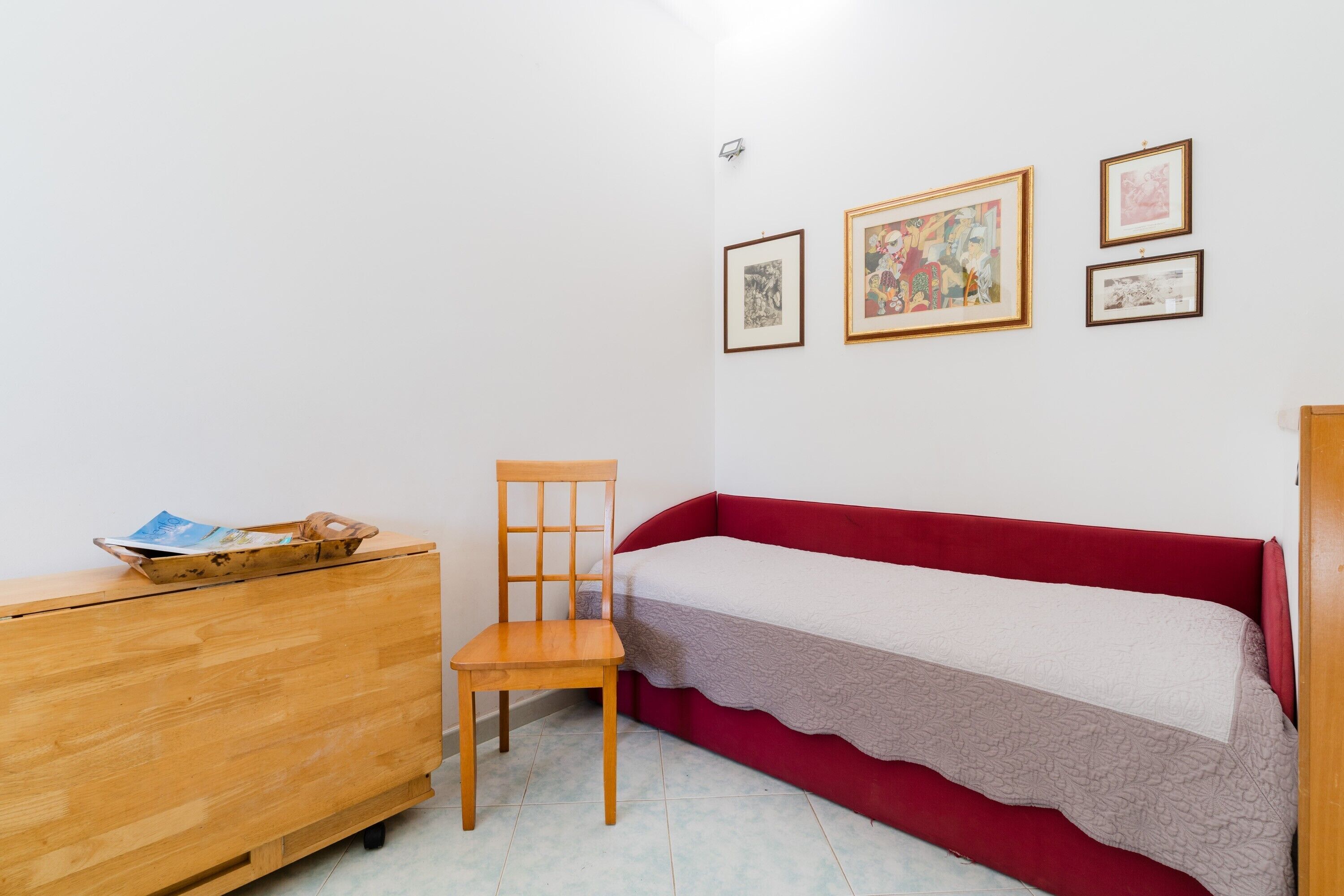 Een kleine kamer met een houten dressoir, een rode bank en drie ingelijste foto’s aan de muur.