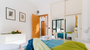 Una habitación de hotel moderna con una cama, un escritorio, una silla, un aparador blanco y dos cuadros en la pared.