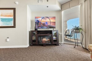 A living room with a fireplace, a television mounted on a wooden cabinet, and a balcony with a view of the ocean. - Crescent Shores #1607S - Oceanfront 3BD - Indoor/Outdoor Pools (North Myrtle Beach,)