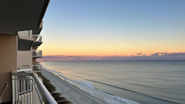 Ein Balkon mit Blick auf einen Strand und den Ozean im Sonnenuntergang.