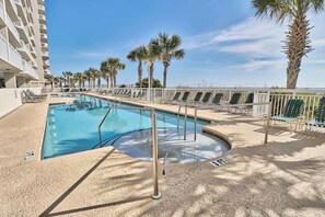 A pool area with lounge chairs, palm trees, and a building in the background. - Crescent Shores #1607S - Oceanfront 3BD - Indoor/Outdoor Pools (North Myrtle Beach,)
