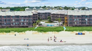 Ein Strandhotel mit mehreren Balkonen, einem Poolbereich und einem Sandstrand.