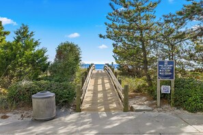 Ein hölzerner Steg führt zu einem Strand, mit einem 'Pay to Park'-Schild und einem QR-Code für Zahlungsoptionen.