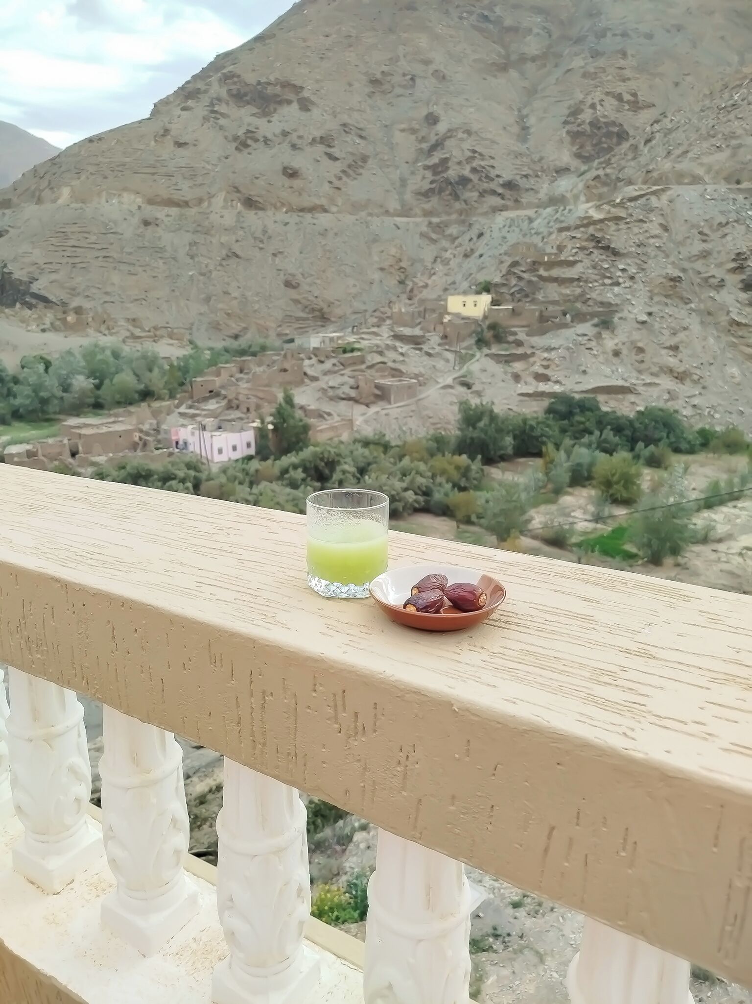 Ein Balkon mit einem Glas grünem Saft und einer Schale Datteln.