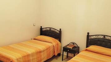 Een kamer met twee bedden, elk met een donker hoofdbord en beddengoed met oranje strepen. Er staat een klein nachtkastje met een boek erop.