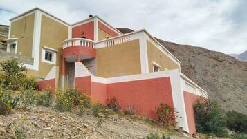 Ein mehrstöckiges Gebäude mit roter und beiger Fassade, einem Balkon und einem Bergpanorama.