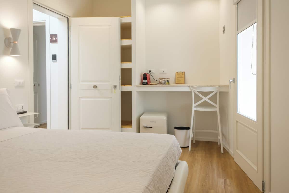 Ein Schlafzimmer mit einem Bett, einem Schreibtisch, einem Stuhl, einem Mülleimer und einem Fenster.