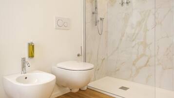 A bathroom with a bidet, a toilet, and a shower with a glass door.