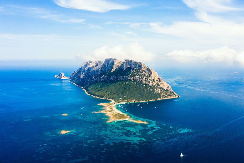 An aerial view of a rugged island with a clear coastline, surrounded by deep blue waters.