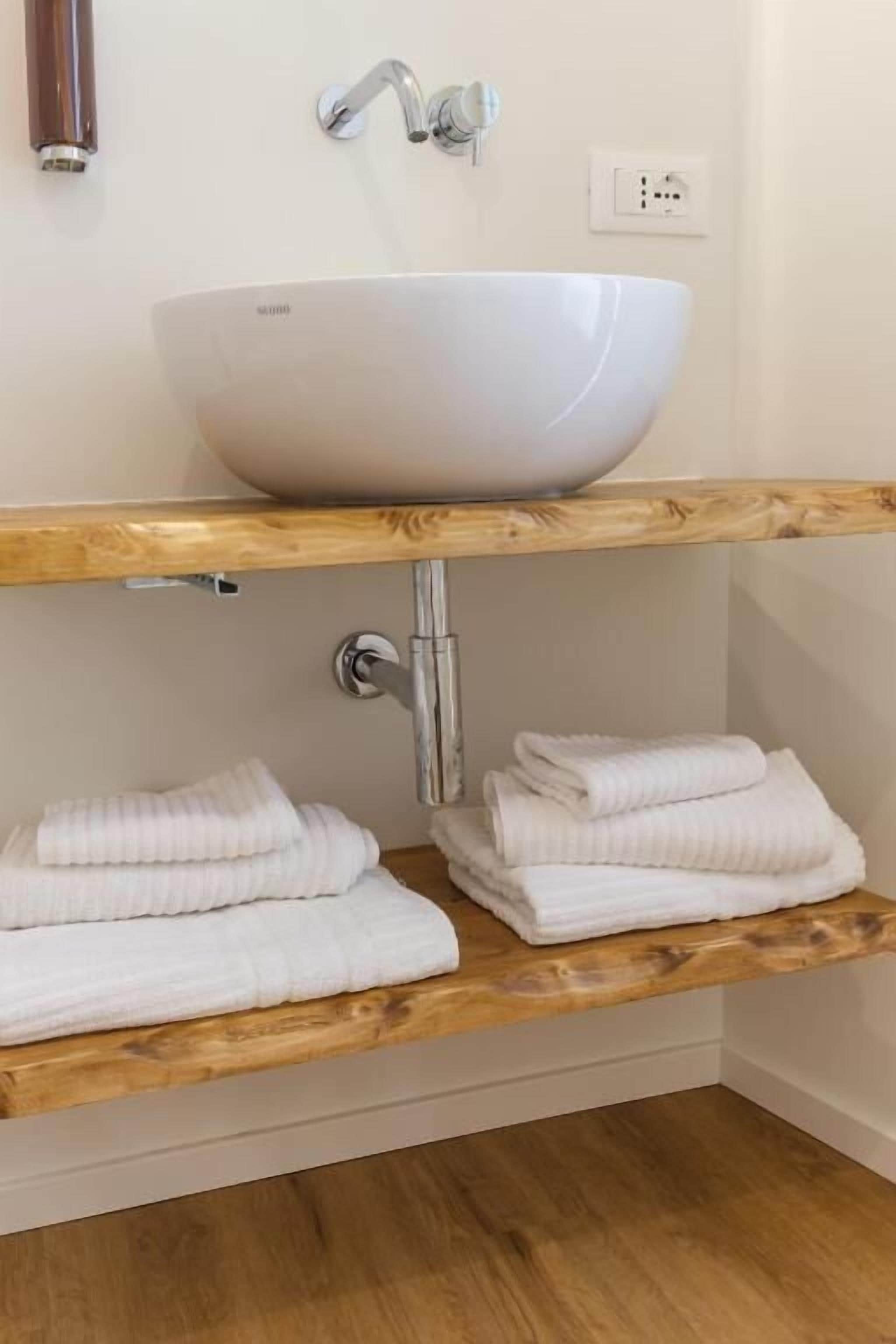 Une salle de bain avec un lavabo sur colonne blanc, des étagères en bois et des serviettes soigneusement pliées.