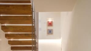 A modern staircase with wooden steps and a metal railing, leading to a landing with a light fixture.