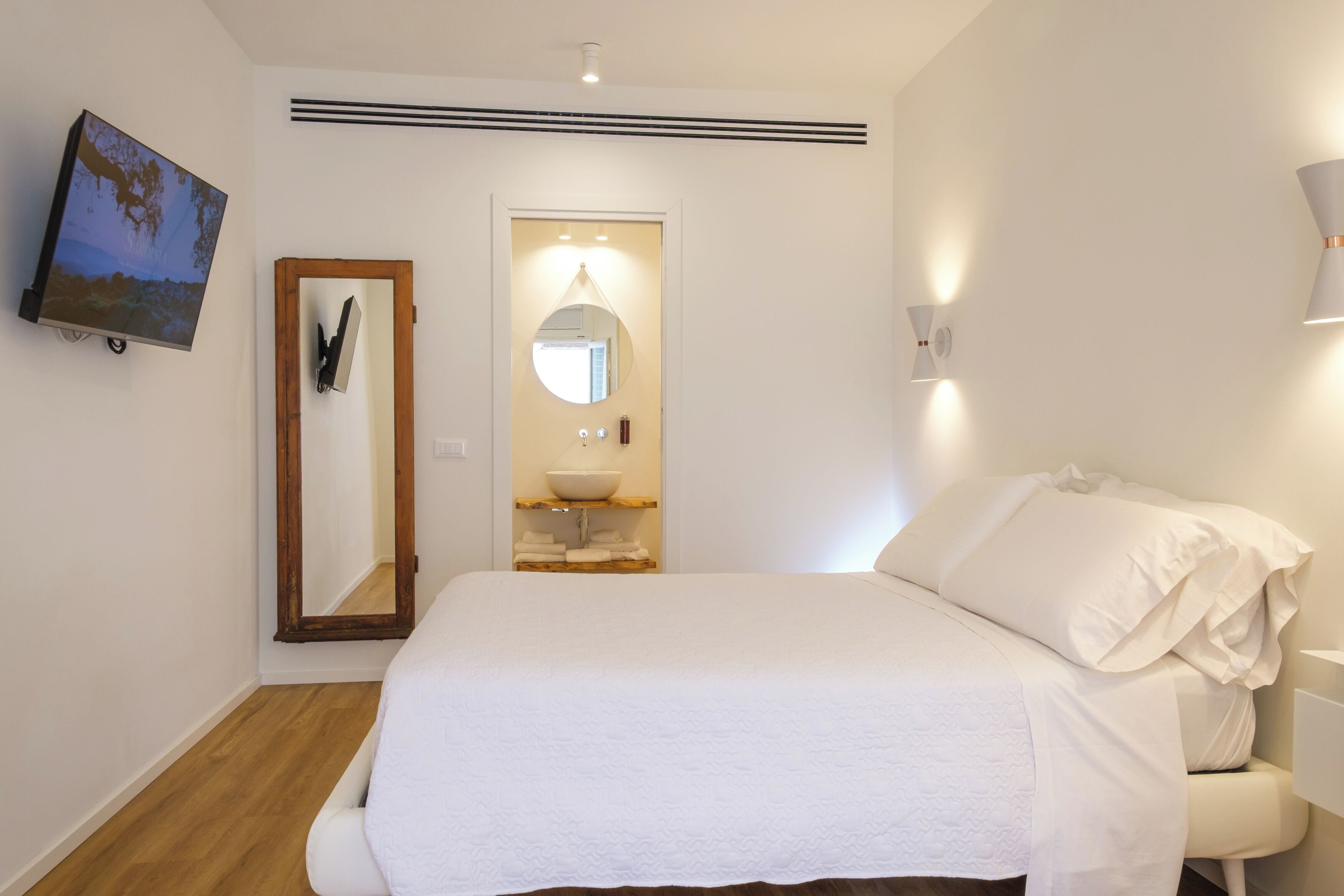 Een slaapkamer met een bed, een spiegel, een wastafel en een televisie.