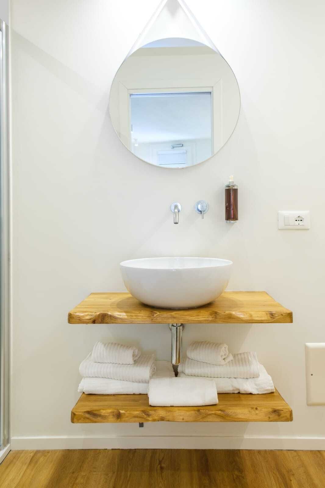 A bathroom with a white sink, wooden shelves, a round mirror, and a towel rack.