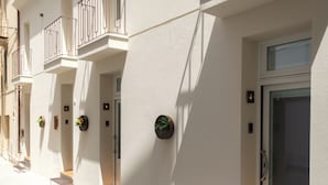 A building facade with multiple balconies, potted plants, and numbered doors.