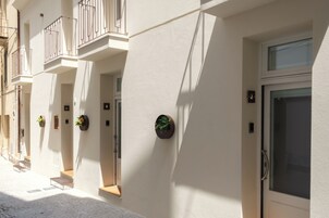 Une façade d’immeuble ornée de nombreux balcons, de plantes en pot et de portes numérotées.