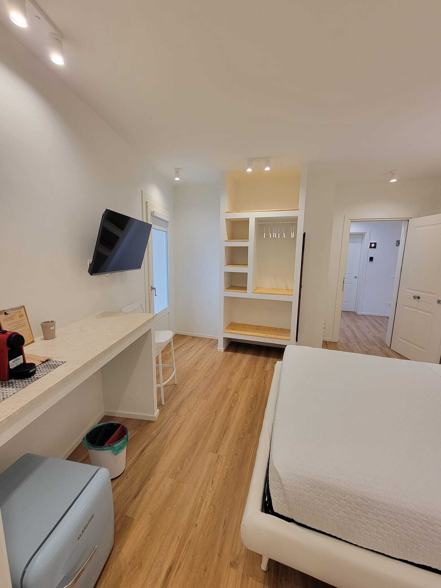 A bedroom with a bed, a desk with a computer, a TV, and a wardrobe.