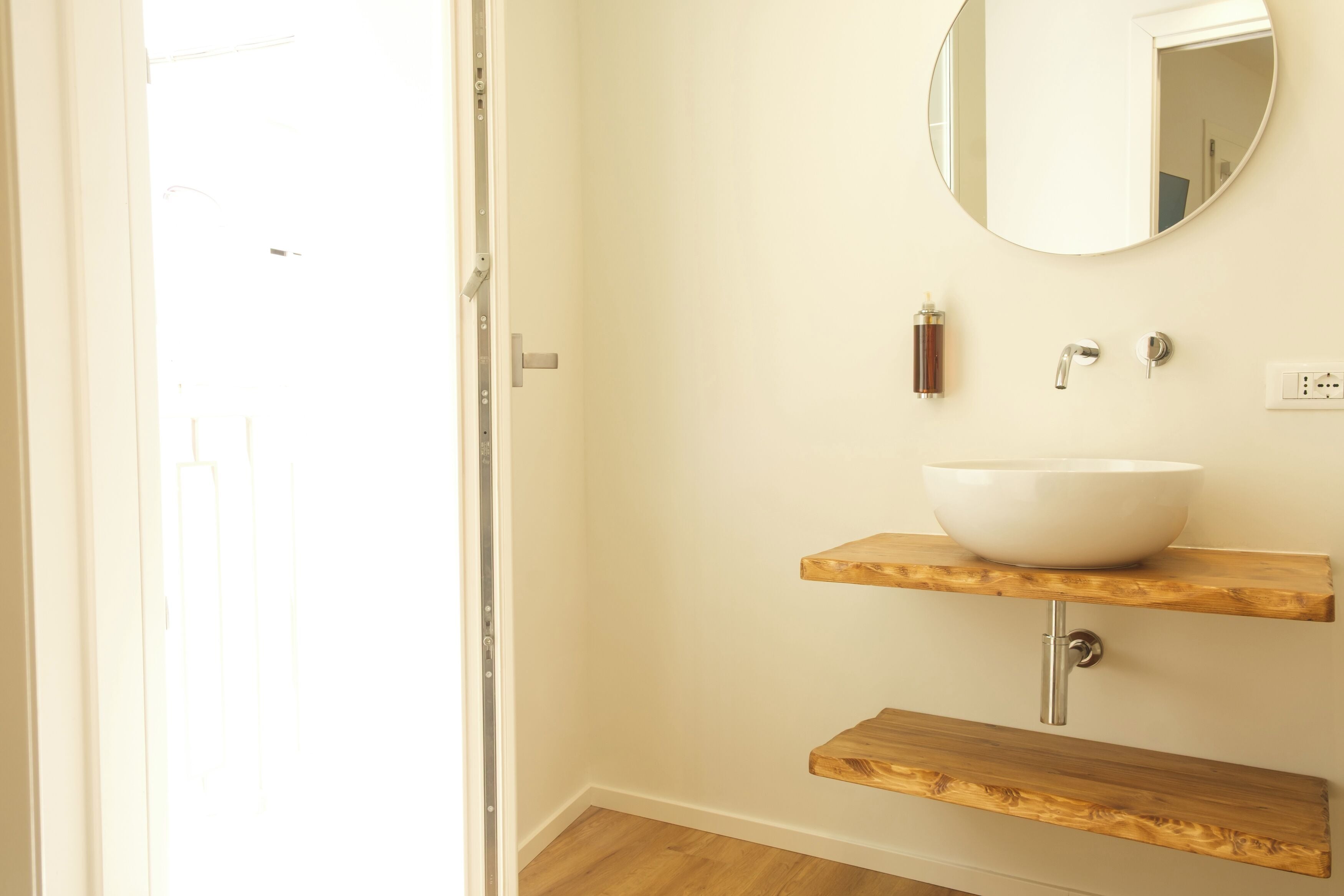 Ein Badezimmer mit einem weißen Waschbecken auf einem Holzregal, einem runden Spiegel darüber und einem Holzrahmen an der Tür.