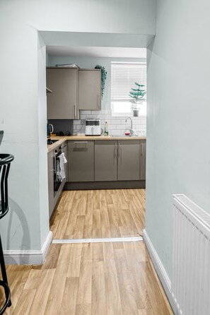 A kitchen with grey cabinets, a toaster, a kettle, and a window with blinds. - Private entrance, full kitchen and quick tram ride to Manchester (Chorlton-cum-Hardy)