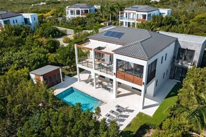 Una casa moderna de dos pisos con piscina, paneles solares y un jardín cuidado.