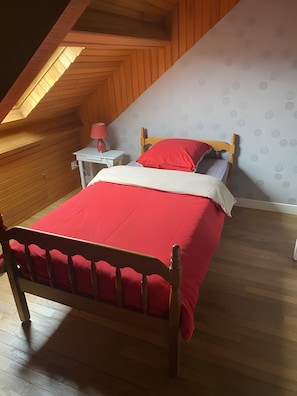 Un dormitorio con techo inclinado, una cama con colcha roja, una mesita de noche con lámpara y una pared con diseños circulares.