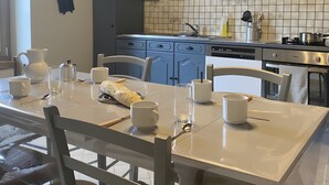 Een moderne keuken met grijze kastjes, een betegelde spatwand en een eethoek met een witte tafel en stoelen.