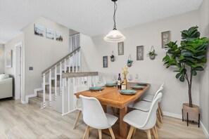 A dining area with a wooden table, white chairs, and a hanging light fixture. - Chimney Park Retreat | King Suite, Sleeps 10 (Windsor)