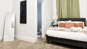 Une chambre à coucher comprenant un lit, une table de chevet, une lampe, une fenêtre avec des rideaux verts, une porte et un climatiseur fixé au mur.