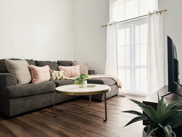 A living room with a grey sofa, a round coffee table, and a TV on a stand. - The Harrison D - QUEEN 1BD/1BA Apt near River (Evansville)
