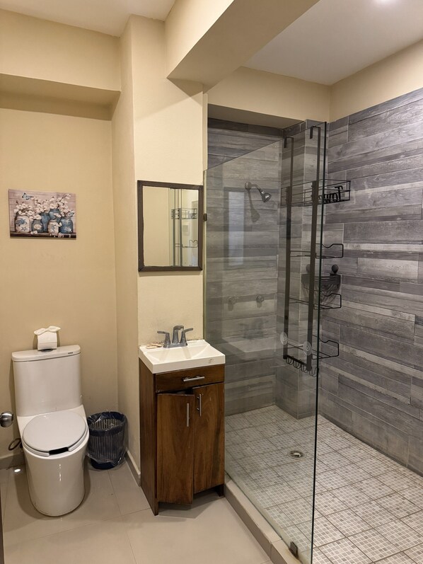Un baño moderno con inodoro, lavamanos y cabina de ducha de vidrio.