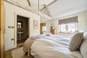 A bedroom with a bed, a window with a valance, a mirror, and a door leading to a bathroom. - 3 Marshland Barns - sleeps 8 guests  in 4 bedrooms (Titchwell)