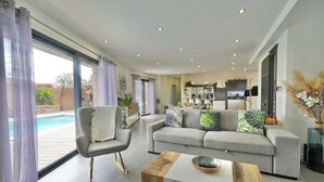 A modern living room with a grey sofa, a wooden coffee table, and a view of a swimming pool through large windows. - Villa 10 people with swimming pool - Lecci (Lecci)