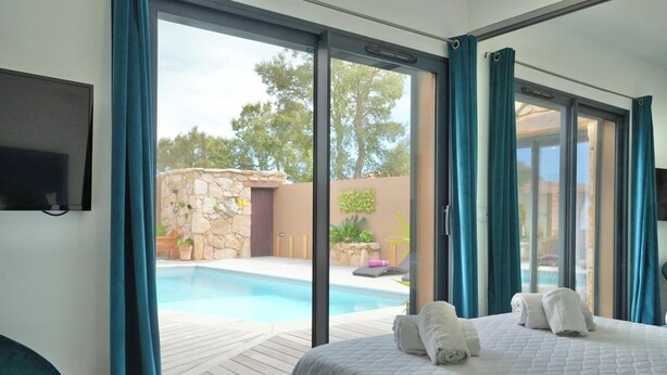 A bedroom with a large bed, a TV mounted on the wall, and a view of an outdoor swimming pool through large sliding glass doors. - Villa 10 people with swimming pool - Lecci (Lecci)