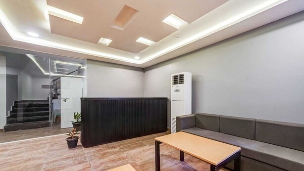 A modern office space with a reception area, a sofa, a table, and a staircase leading to an upper floor.