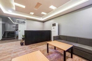 Een moderne kantoorruimte met een receptiehoek, een bank, een tafel en een trap naar een verdieping boven.