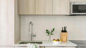 Una cucina moderna con lavello in acciaio inox, un forno a microonde e una ciotola di frutta sul piano di lavoro.